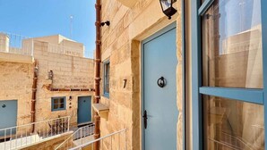 A building with a light blue door, a balcony with a metal railing, and a window with a metal grid. - Kappella Boutique - Room 4 (Zurrieq)