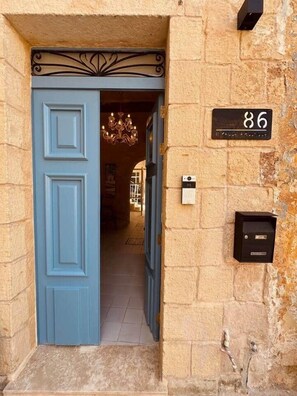 A fachada de um edifício de pedra com uma porta azul, uma placa de número e uma caixa de correio.