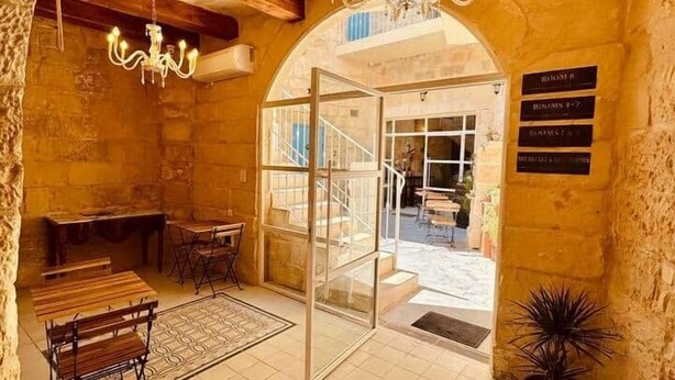 Una stanza con pareti in pietra, un lampadario, un tavolo con sedie e una targa con i numeri delle camere.