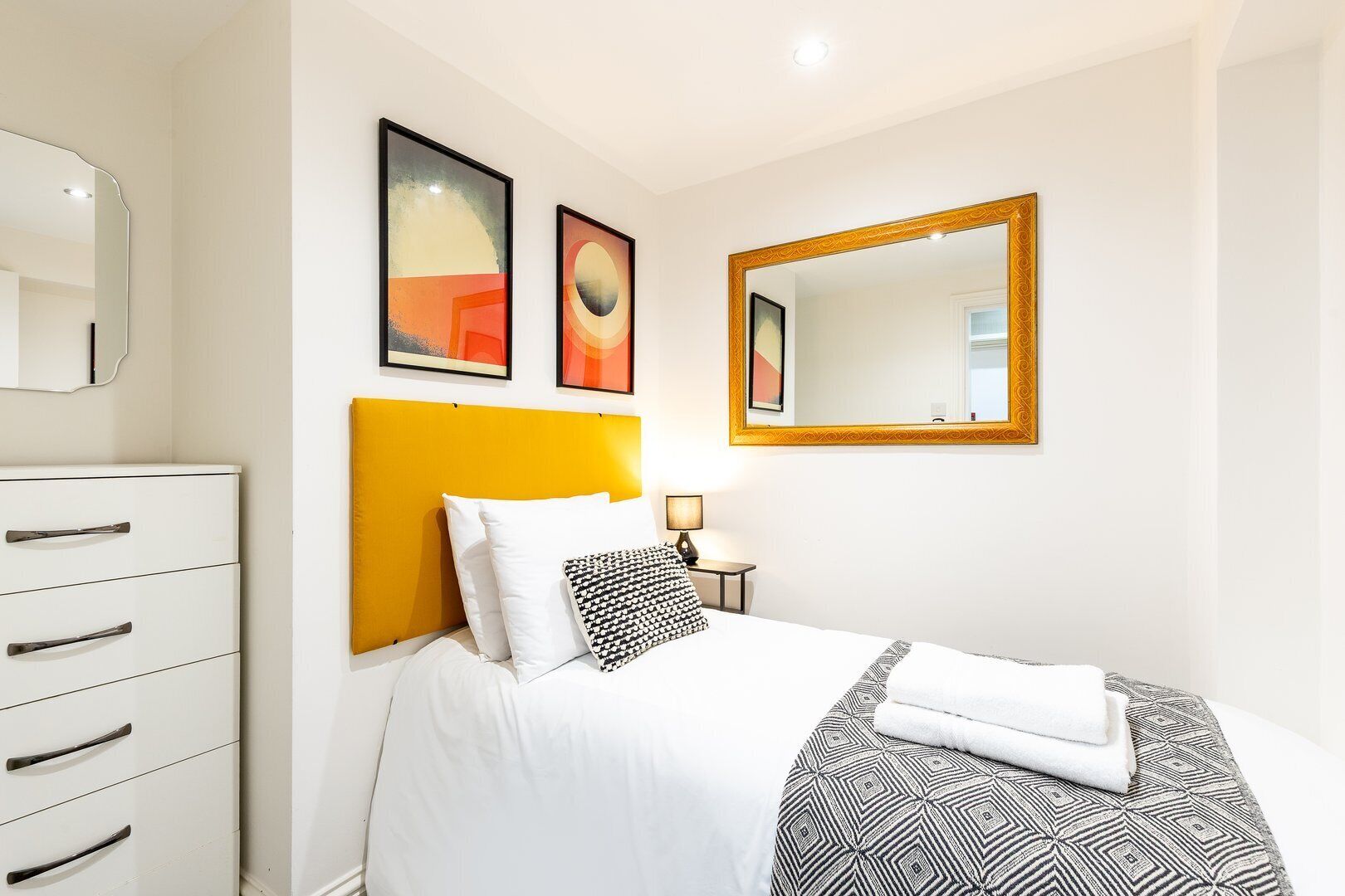 Une chambre d’hôtel avec un lit, une commode et deux œuvres d’art encadrées accrochées au mur.