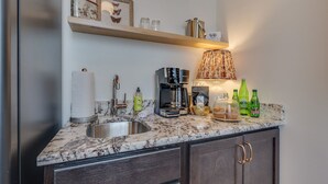 A kitchen with a marble countertop, a coffee maker, a sink, and a shelf with decorative items.