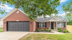 A single-story brick house with a garage, a front porch, and a small front yard with landscaping. - Georgetown Getaway, Sleeps 6, Fenced Yard (Pet-Friendly), Near Lexington & I-75 (Georgetown)