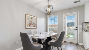 A dining area with a white table, four grey chairs, a chandelier, a framed floral painting, and a window with blinds. - Georgetown Getaway, Sleeps 6, Fenced Yard (Pet-Friendly), Near Lexington & I-75 (Georgetown)