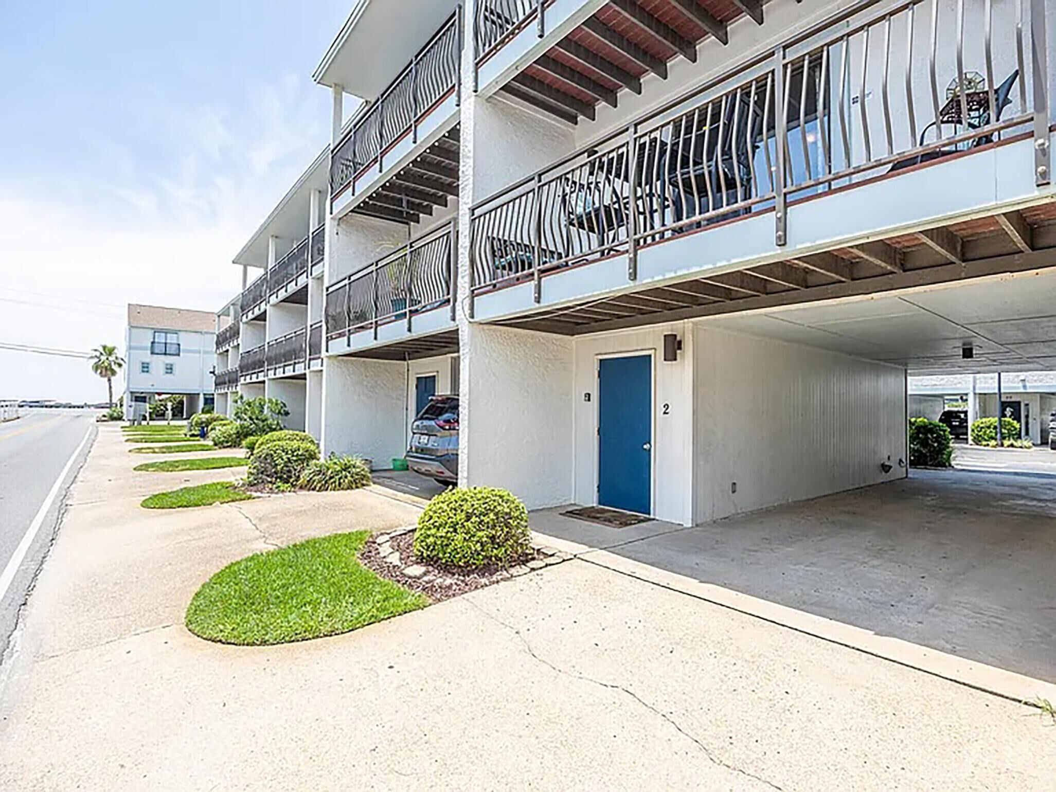 A multi-story parking garage with a blue door, adjacent to a building with balconies and a covered walkway.