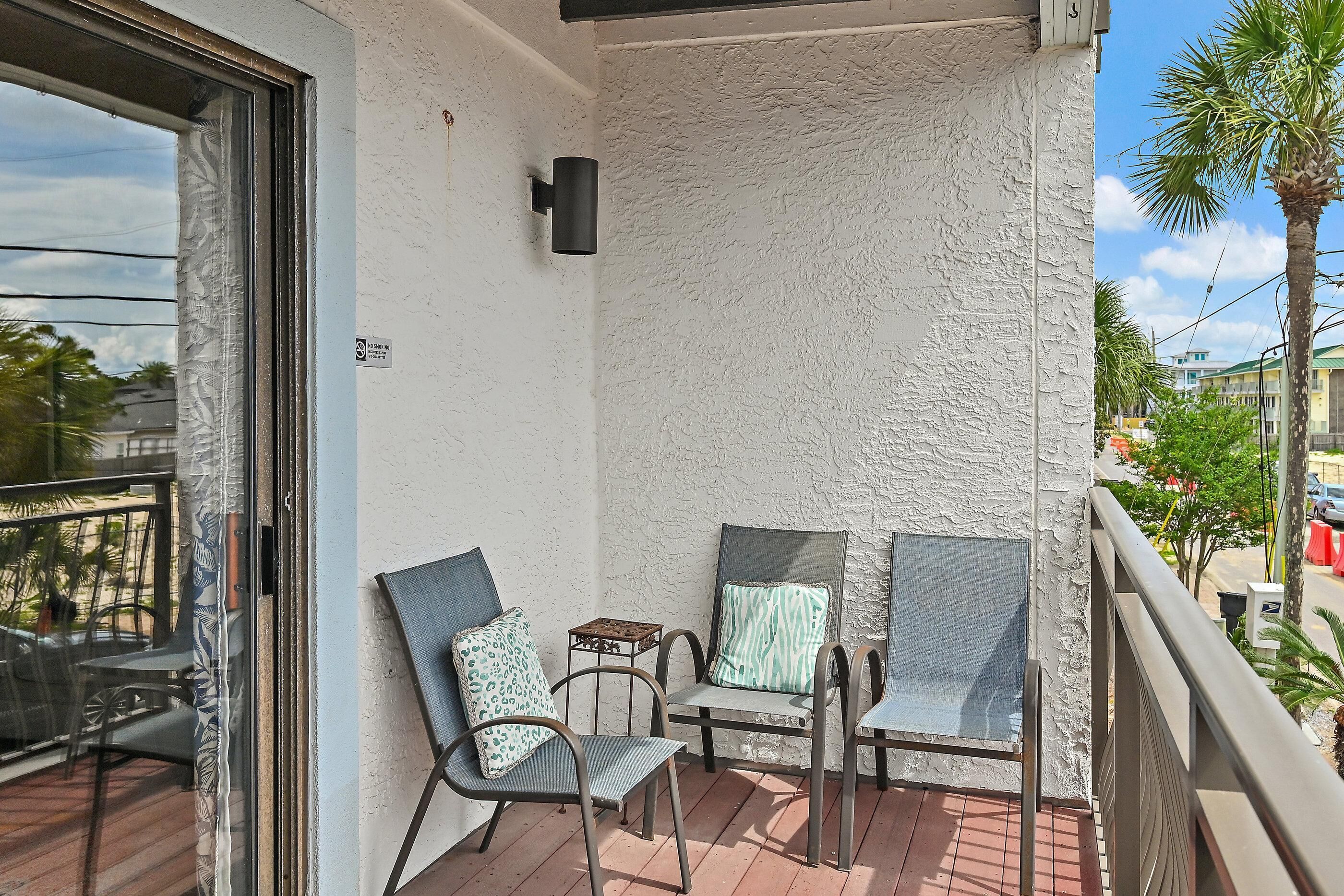 A balcony with two chairs and a small table, a textured wall, and a view of the street.