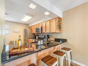Eine moderne Küche mit Holzschränken, einem Edelstahlkühlschrank, einer Mikrowelle und einer zentralen Kochinsel mit Sitzgelegenheiten.