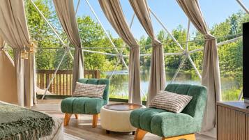 A tented room with two green armchairs, a round table, and a TV on a wooden cabinet.