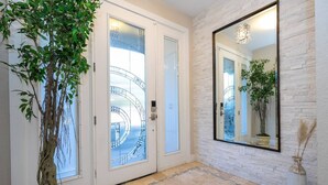 A hallway with a large mirror, a potted tree, and a glass door with a view of a balcony. - 3-Bedroom Luxury House (Orlando)
