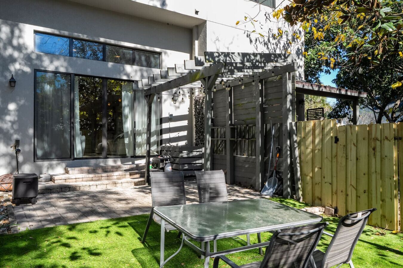A modern patio with a metal table and chairs, a wooden pergola, and a wooden fence.