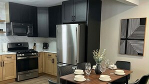 A modern kitchen with dark cabinets, stainless steel appliances, and a dining area with a wooden table and black chairs. - Modern 3BR Home Near Wheaton College & Cantigny (Wheaton)