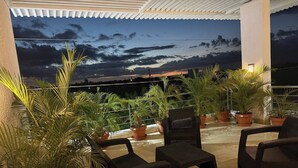 Terraza en la azotea con plantas en macetas, mobiliario exterior y vistas al cielo.