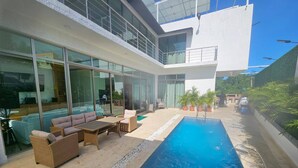 Un área de piscina moderna al aire libre, con sillones, mobiliario de relax y un porche con paredes de cristal.
