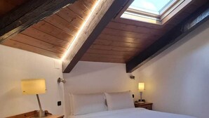 Quarto com claraboia, uma cama, cômoda de madeira e duas luminárias de cabeceira.