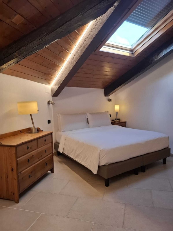 A bedroom with a skylight, a bed, a wooden dresser, and two bedside lamps. - Carafa Suite Plus II (Naples)