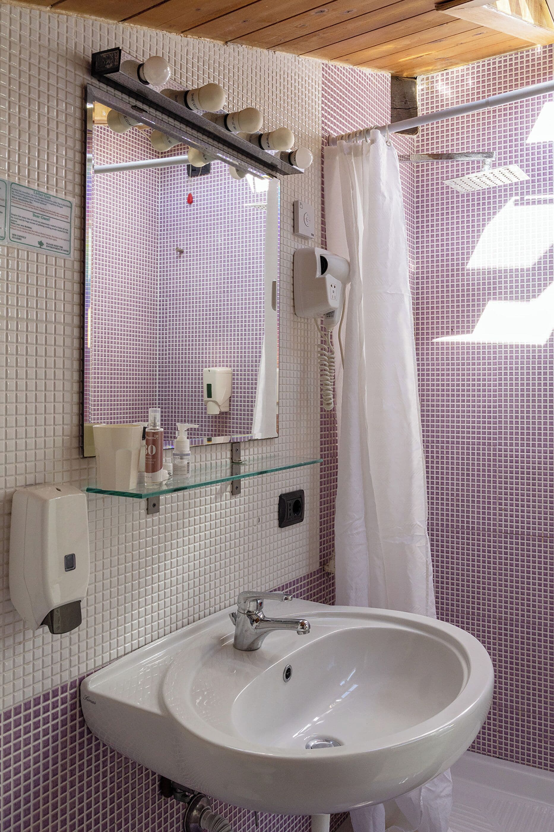 Ein Badezimmer mit weißem Waschbecken, einem Spiegel, einer Glasablage für Toilettenartikel und einer Duschvorhang.