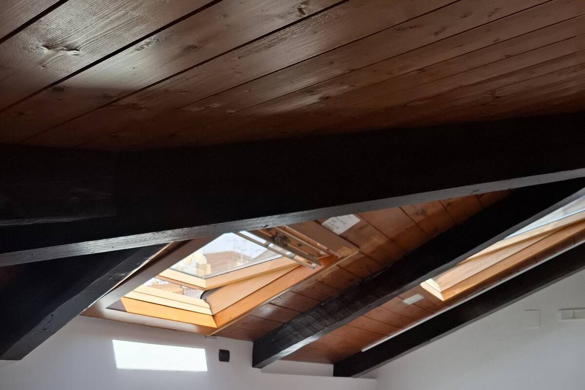 Une chambre aménagée dans les combles, avec un puits de lumière, un lit, un bureau avec des chaises et une petite table ronde.