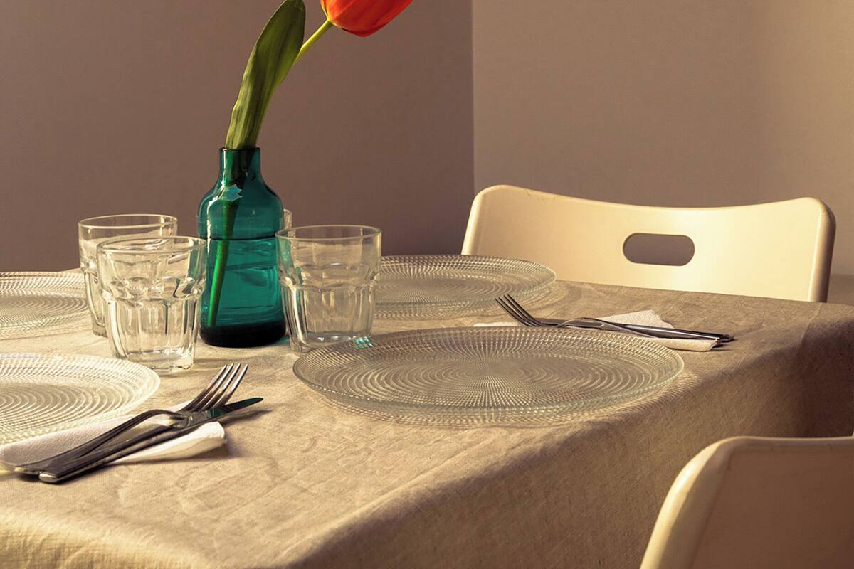 Une table à manger dressée avec un vase contenant une seule tulipe rouge, des verres transparents et des couverts.