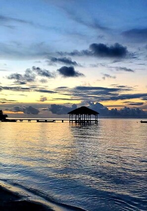A tranquil waterfront scene with a gazebo-like structure on stilts over calm water, surrounded by a dock and distant shoreline. - Peaceful Private Natural Paradise. Private pool. Restaurant & Bar, Dive Shop (Roatan)
