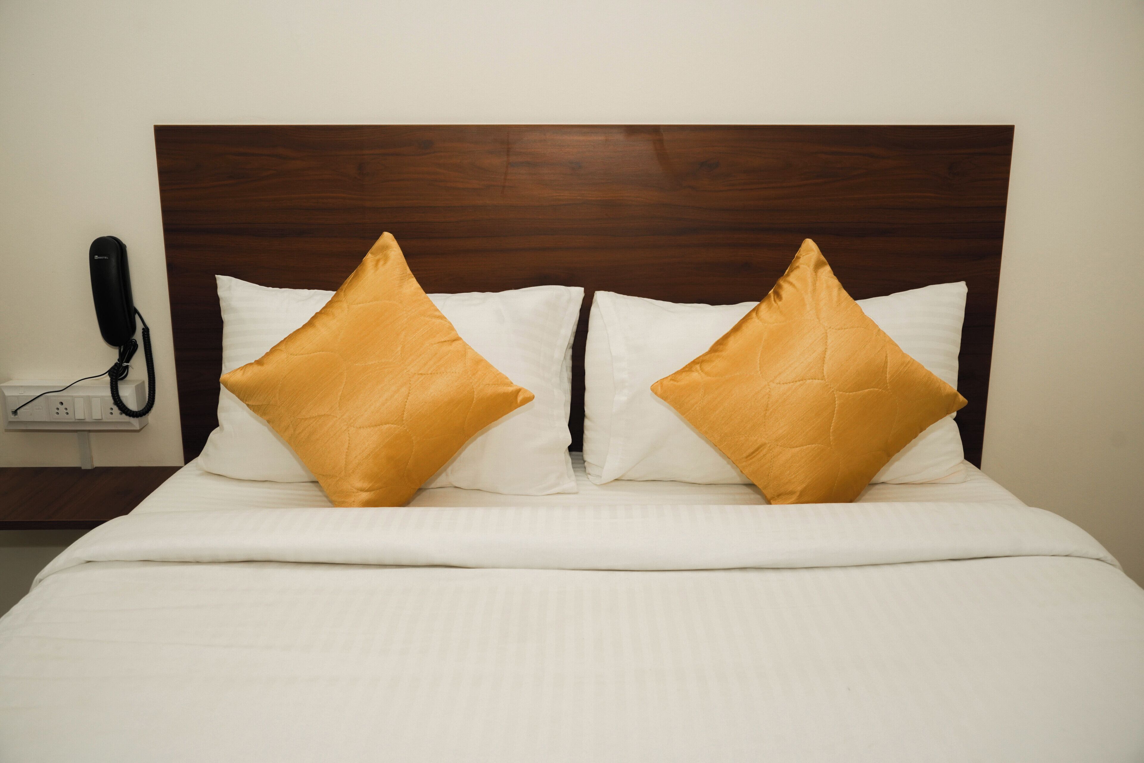 A neatly made bed with white bedding and two gold pillows.