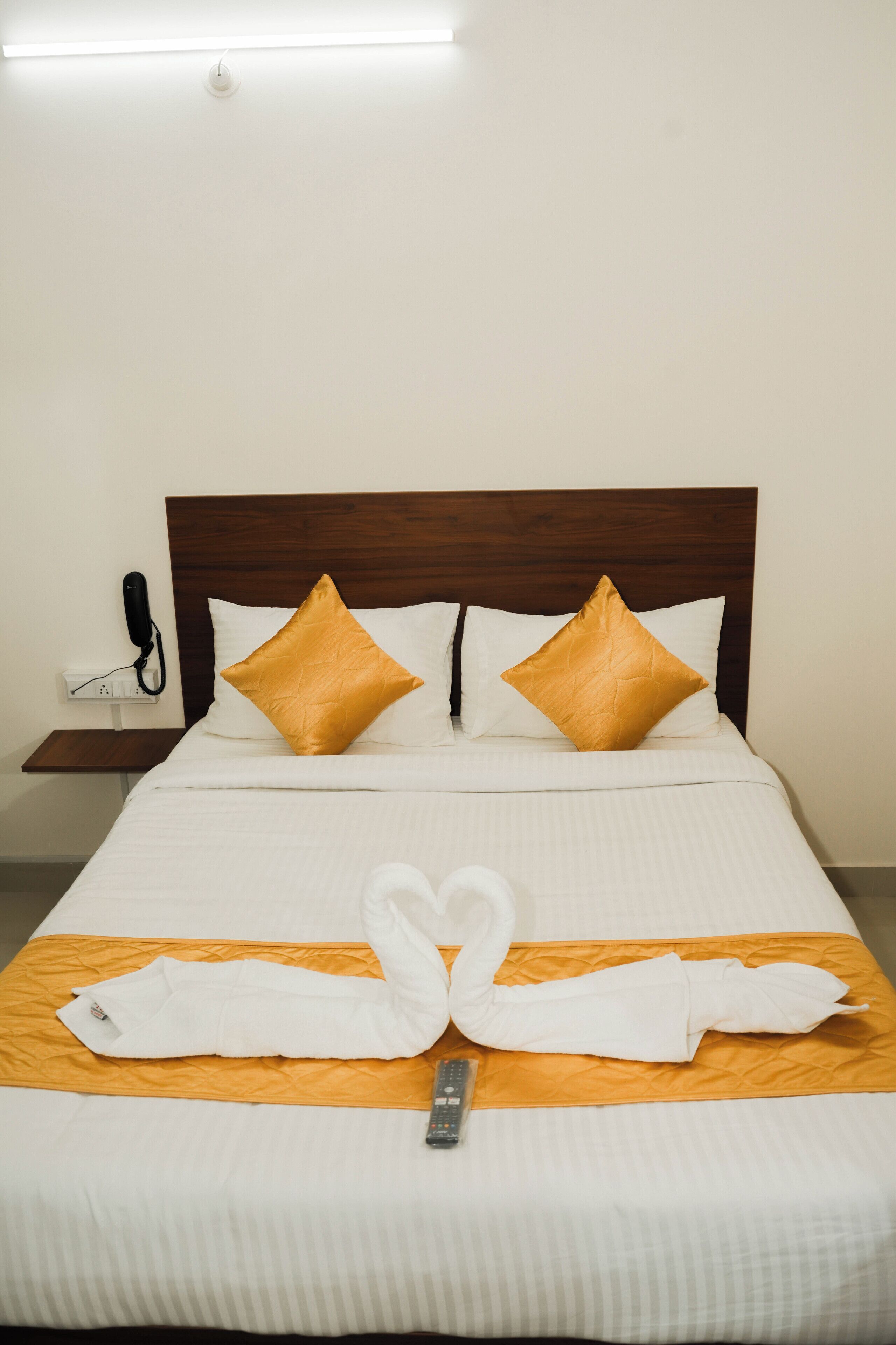 Una cama bien arreglada con un diseño de cisne en la toalla, dos almohadas doradas y un control remoto sobre la cama.