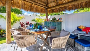 An outdoor patio with a thatched roof, wicker furniture, and a dining table set for four.