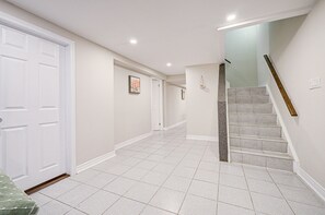 A hallway with a white door, a staircase with a wooden handrail, and a tiled floor. - Entire comfy lower-level classic in Richmond Hill (Richmond Hill)