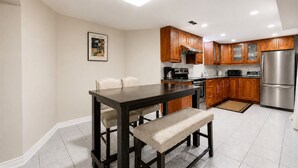 Una cocina moderna con gabinetes de madera, electrodomésticos de acero inoxidable y una zona de comedor con una mesa oscura y sillas acolchadas.