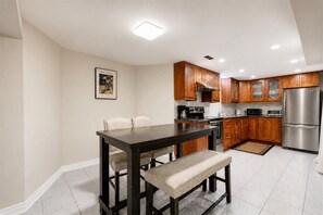 A modern kitchen with wooden cabinets, stainless steel appliances, and a dining area with a dark table and cushioned chairs. - Lower-level house in peaceful Richmond Hill with AC and charm (Richmond Hill)