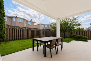 A covered patio with a table and chairs, a wooden fence, and a well-maintained lawn.