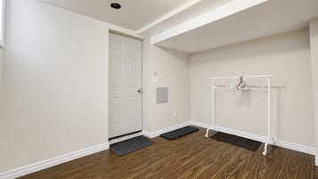 Une pièce avec un plancher en bois, une porte blanche, un porte-manteau avec des cintres et un petit paillasson à l’entrée.