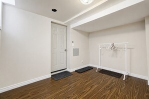 Ein Zimmer mit Holzboden, einer weißen Tür, einem Kleiderhaken mit Kleiderbügeln und einer kleinen Fußmatte am Eingang.