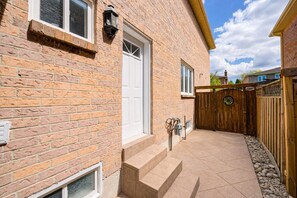 A brick house with a white door, a wooden fence, and a paved patio.