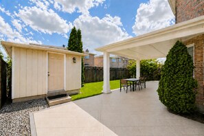 A covered patio area with a table and chairs, a small shed, and a well-maintained lawn.