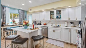 A modern kitchen with white cabinets, a central island with stools, a sink, and a refrigerator. - Heated Pool, Putt-Putt, Billiards, Ping Pong, Bar (Lighthouse Point)