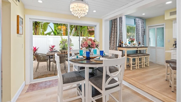 A dining area with a chandelier, a table set for four, and a view of the garden through the glass door. - Heated Pool, Putt-Putt, Billiards, Ping Pong, Bar (Lighthouse Point)