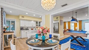 A dining area with a round table, chairs, and a vase of flowers. There is a pool table in the background. - Heated Pool, Putt-Putt, Billiards, Ping Pong, Bar (Lighthouse Point)