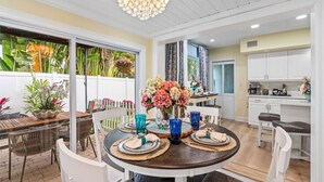 A dining area with a round table set for four, surrounded by white chairs. A chandelier hangs from the ceiling, and the room has a white and yellow color scheme. - Heated Pool, Putt-Putt, Billiards, Ping Pong, Bar (Lighthouse Point)