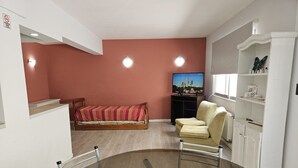 Um espaço de estar compacto com cama, sofá, televisão e área de refeições com mesa de vidro.