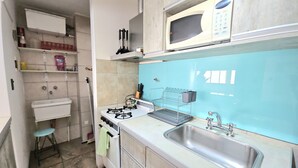 Uma cozinha compacta com fogão a gás, micro-ondas, pia e um banquinho pequeno.