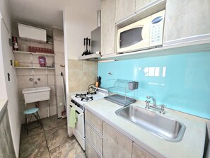 A compact kitchen with a gas stove, a microwave, a sink, and a small stool. - Civic center Bariloche (San Carlos de Bariloche)