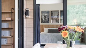 A modern hotel room with a bed, a dining area with a table and chairs, a vase with flowers, and a large window with a view of mountains. - Ridgeline Penthouse (Revelstoke)