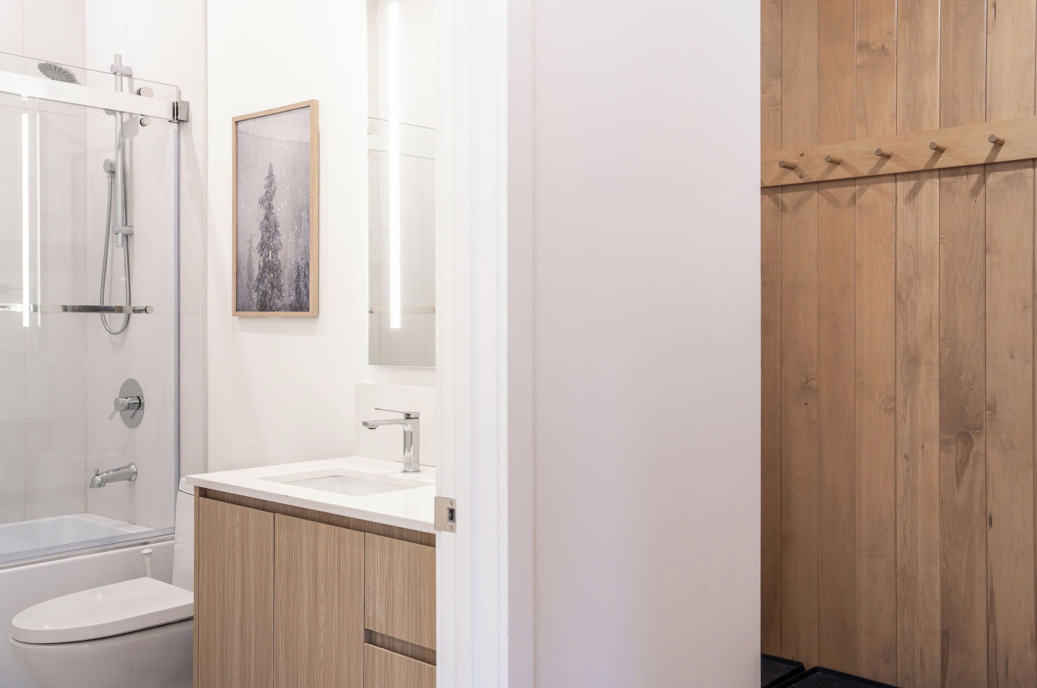 Un baño moderno con cabina de ducha de vidrio, lavamanos blanco y muebles de madera.