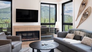 A modern living room with a fireplace, a flat-screen TV, and a sofa with a view of mountains. - Ridgeline Penthouse (Revelstoke)