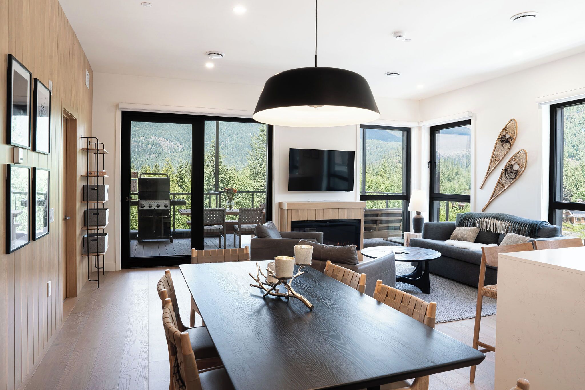 A modern interior with a dining area, sofas, a fireplace, and large windows offering a view of the outdoors.