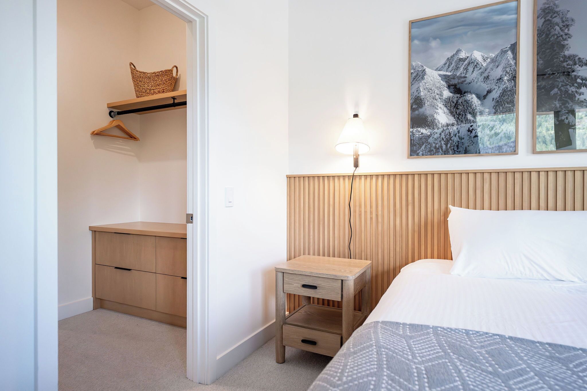 A bedroom with a bed, a bedside table, a nightstand, a hanging basket, and a wall-mounted lamp.