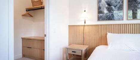 A bedroom with a bed, a bedside table, a nightstand, a hanging basket, and a wall-mounted lamp.