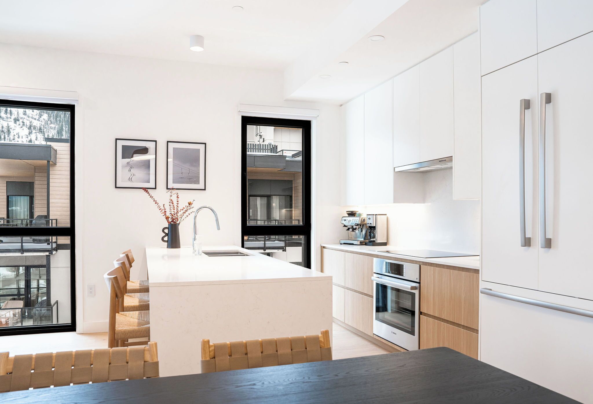 Een moderne keuken met een centraal eiland, roestvrijstalen apparatuur en uitzicht op de natuur.