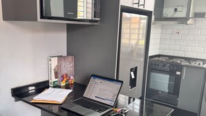 Une cuisine moderne équipée d’un four à micro-ondes, d’un réfrigérateur et d’une cuisinière intégrés. On y trouve un ordinateur portable sur un plan de travail noir, ainsi qu’une chaise et une petite table à proximité.