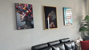 Un salon moderne avec un canapé en cuir noir, trois œuvres d’art encadrées accrochées au mur et une grande plante verte.