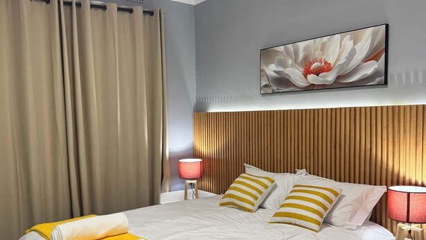 Une chambre d’hôtel comprenant un lit, une table de chevet, une lampe, un climatiseur et une œuvre d’art accrochée au mur.
